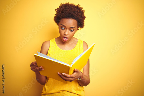 African american woman reading a book over yellow isolated background scared in shock with a surprise face, afraid and excited with fear expression