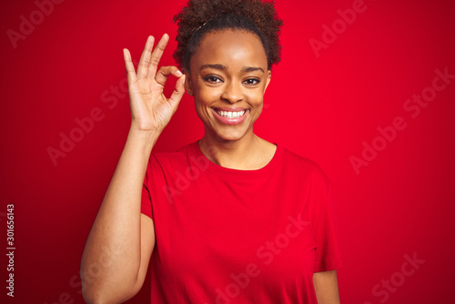 Young beautiful african american woman with afro hair over isolated red background smiling positive doing ok sign with hand and fingers. Successful expression.