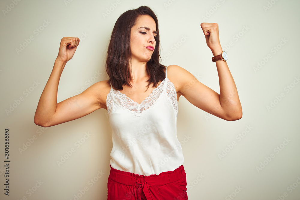Young beautiful woman wearing t-shirt standing over white isolated background showing arms muscles smiling proud. Fitness concept. Young beautiful woman wearing t-shirt standing over white isolated background showing arms muscles smiling proud. Fitness concept.