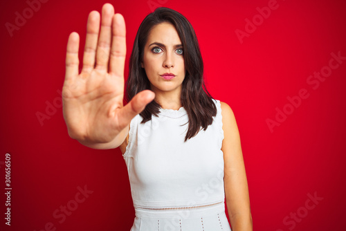 Young beautiful woman wearing white dress standing over red isolated background doing stop sing with palm of the hand. Warning expression with negative and serious gesture on the face.