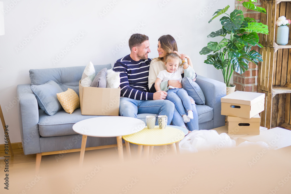 Beautiful family with kid sitting on the sofa drinking coffee at new home around cardboard boxes Beautiful family with kid sitting on the sofa drinking coffee at new home around cardboard boxes