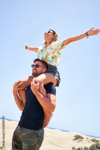 Young beautiful couple smiling happy and confident. Woman sitting on man shoulders with smile on face at the beach