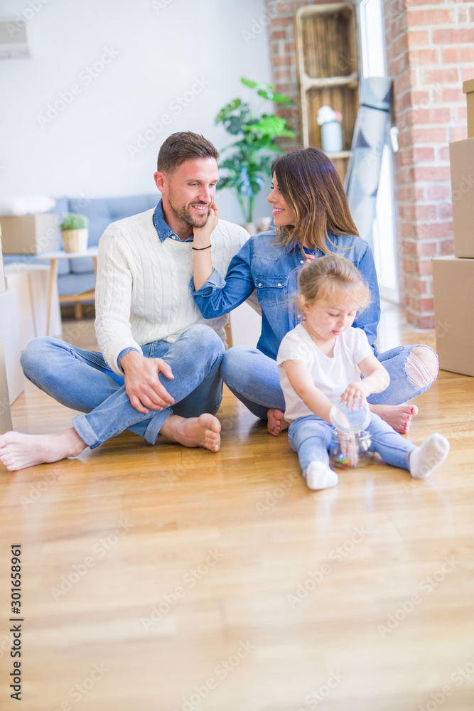 Beautiful family sitting on the floor playing with his kid at new home around cardboard boxes