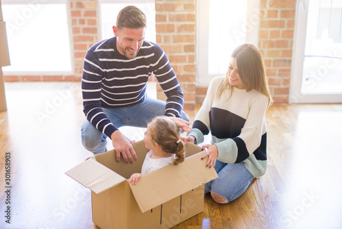 Beautiful famiily, kid playing with his parents riding cardboard fanny box at new home photo