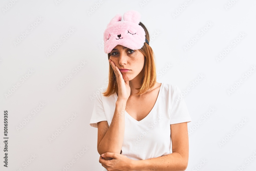 Beautiful redhead woman wearing sleeping mask over isolated background thinking looking tired and bored with depression problems with crossed arms. Beautiful redhead woman wearing sleeping mask over isolated background thinking looking tired and bored with depression problems with crossed arms.