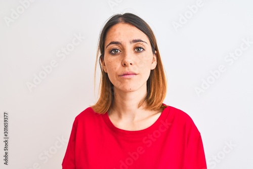 Beautiful redhead woman wearing casual red t-shirt over isolated background Relaxed with serious expression on face. Simple and natural looking at the camera.