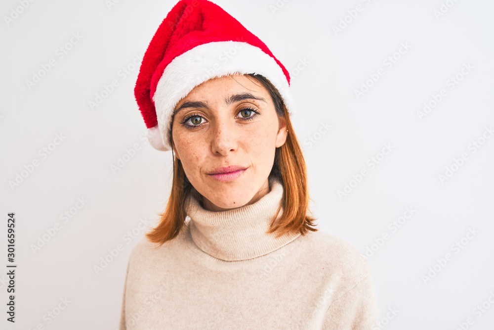 Beautiful redhead woman wearing christmas hat over isolated background with a confident expression on smart face thinking serious Beautiful redhead woman wearing christmas hat over isolated background with a confident expression on smart face thinking serious
