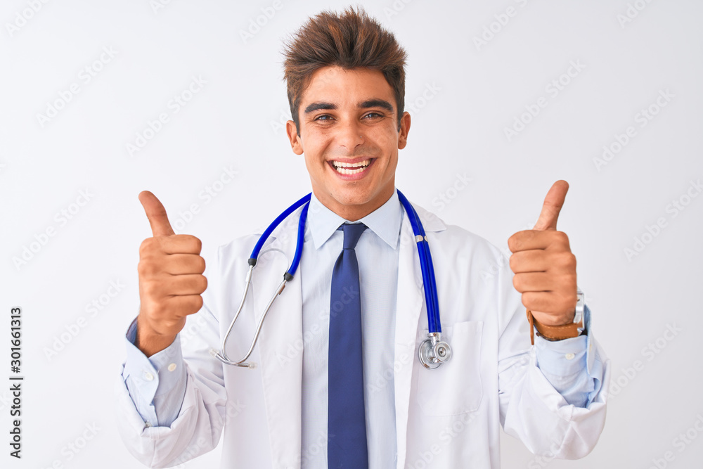 Young handsome doctor man wearing stethoscope over isolated white background success sign doing positive gesture with hand, thumbs up smiling and happy. Cheerful expression and winner gesture. Young handsome doctor man wearing stethoscope over isolated white background success sign doing positive gesture with hand, thumbs up smiling and happy. Cheerful expression and winner gesture.