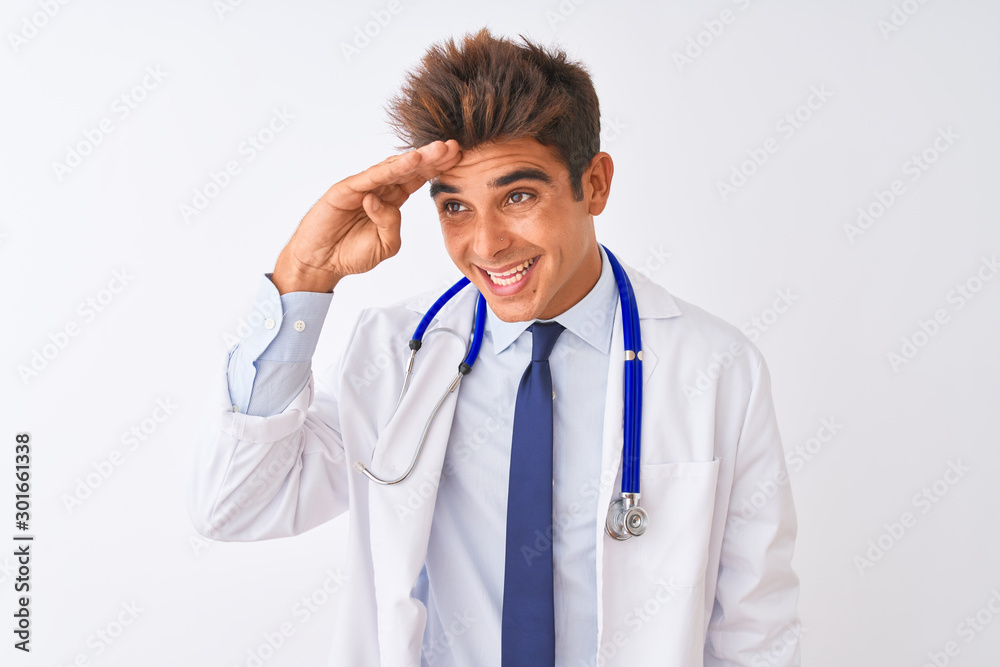 Young handsome doctor man wearing stethoscope over isolated white background very happy and smiling looking far away with hand over head. Searching concept. Young handsome doctor man wearing stethoscope over isolated white background very happy and smiling looking far away with hand over head. Searching concept.