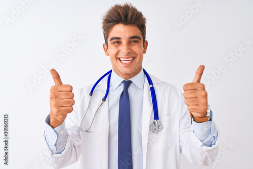 Young handsome doctor man wearing stethoscope over isolated white background success sign doing positive gesture with hand  thumbs up smiling and happy. Cheerful expression and winner gesture.