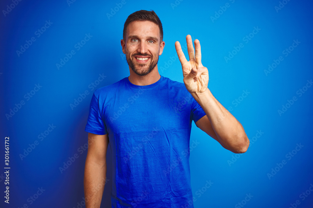 Young handsome man wearing casual t-shirt over blue isolated background showing and pointing up with fingers number three while smiling confident and happy.