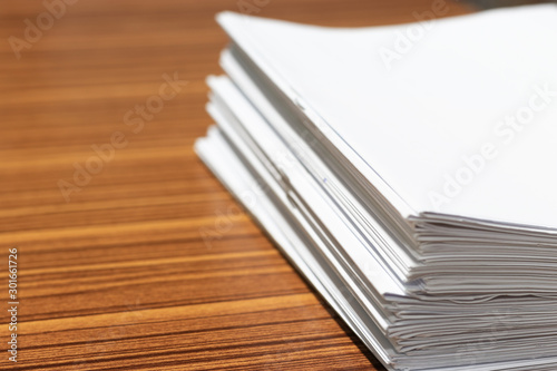 Stack of homework assignment on office wooden desk waiting to be managed and inspected for score. Pile of unfinished paperwork. Report and notebook papers stacked. Business and education concept.