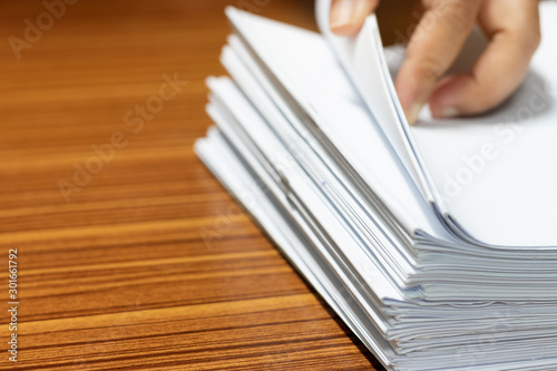 Teacher searching homework assignment on wood desk in school office for score  managed and inspected. Pile of unfinished paperwork. Report and notebook papers stacked. Business and education concept.