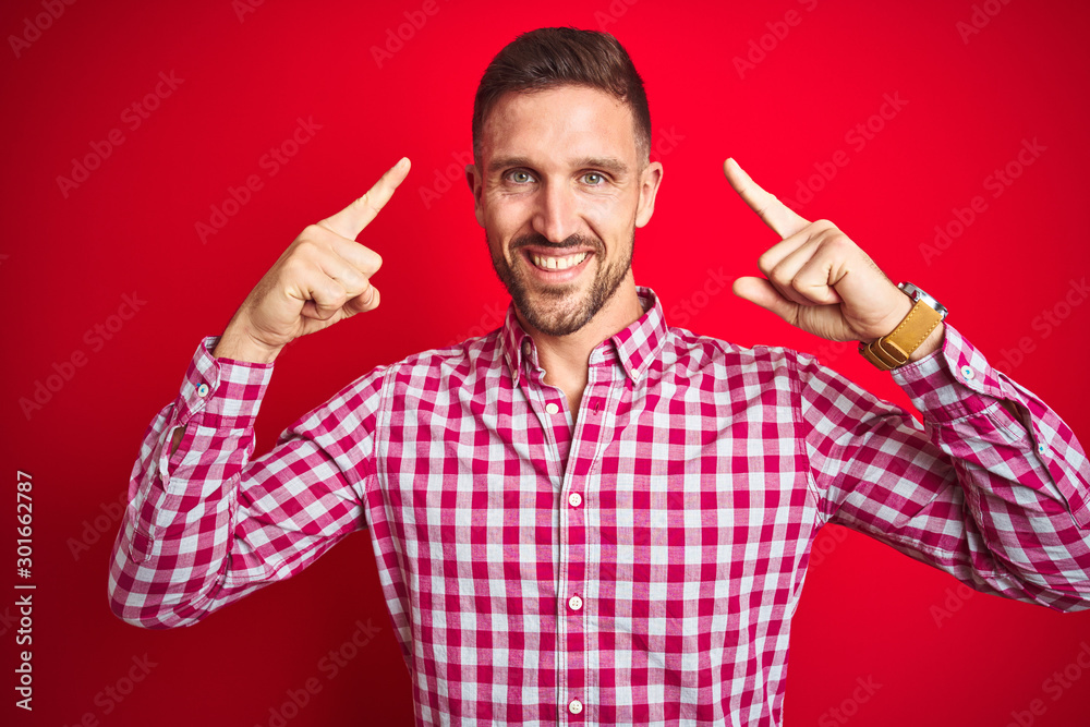 Naklejka premium Young handsome man over red isolated background smiling pointing to head with both hands finger, great idea or thought, good memory