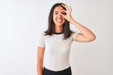 Young beautiful chinese woman wearing casual t-shirt standing over isolated white background doing ok gesture with hand smiling, eye looking through fingers with happy face.