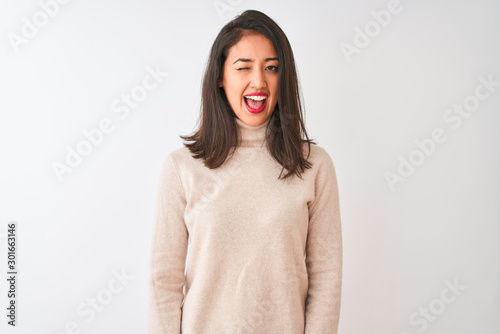 Beautiful chinese woman wearing turtleneck sweater standing over isolated white background winking looking at the camera with sexy expression, cheerful and happy face.