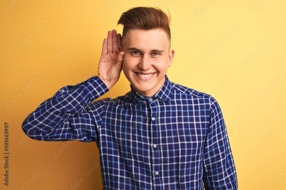 Young handsome man wearing casual shirt standing over isolated yellow background smiling with hand over ear listening an hearing to rumor or gossip. Deafness concept. Young handsome man wearing casual shirt standing over isolated yellow background smiling with hand over ear listening an hearing to rumor or gossip. Deafness concept.