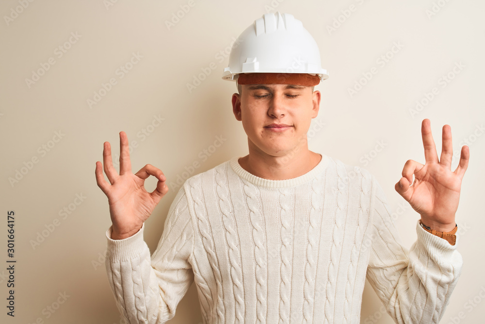 Handsome architect man wearing security helmet standing over isolated white background relax and smiling with eyes closed doing meditation gesture with fingers. Yoga concept.