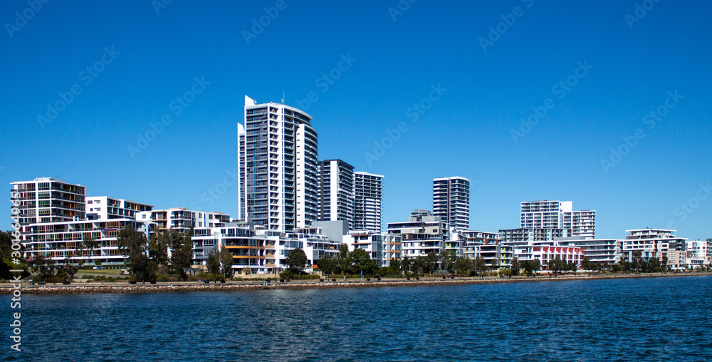 Large waterfront houses, apartment condominiums in suburban community on harbour with tree lined walkway, blue sky in background
