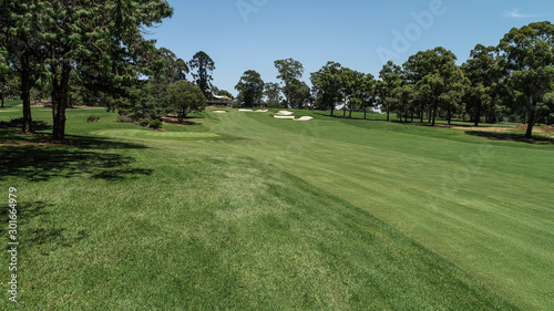 Golf course fairway, sand bunkers, lush green grass surrounded by trees against blue sky