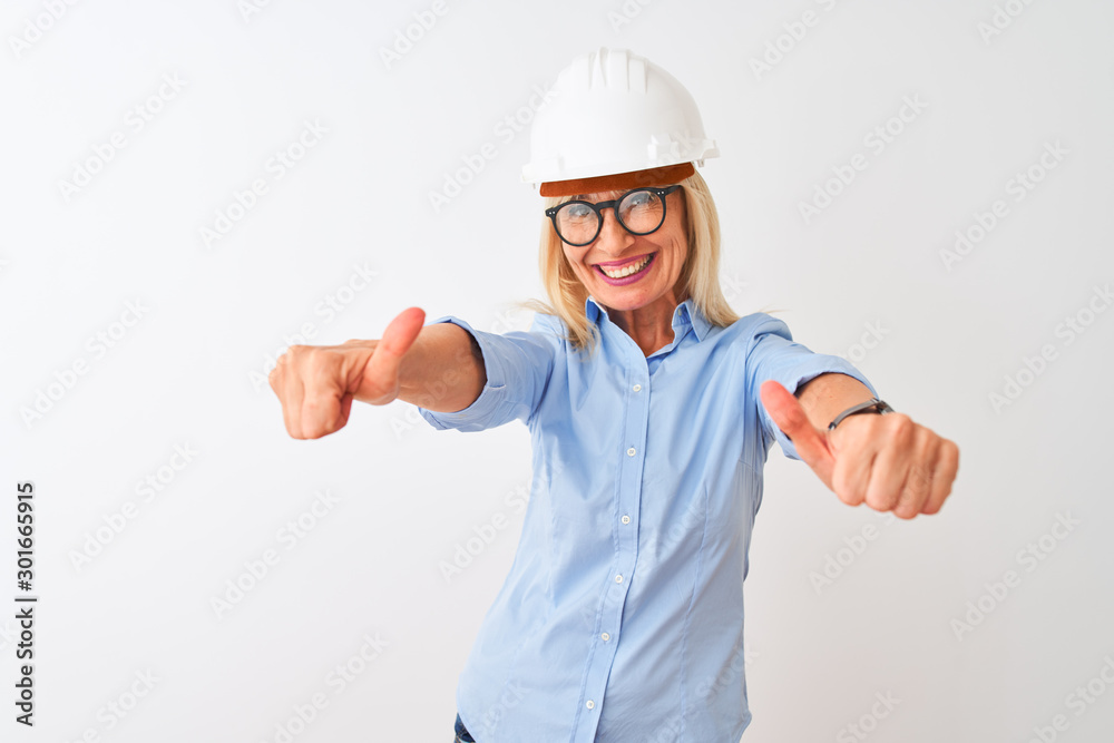 Middle age architect woman wearing glasses and helmet over isolated white background approving doing positive gesture with hand, thumbs up smiling and happy for success. Winner gesture.