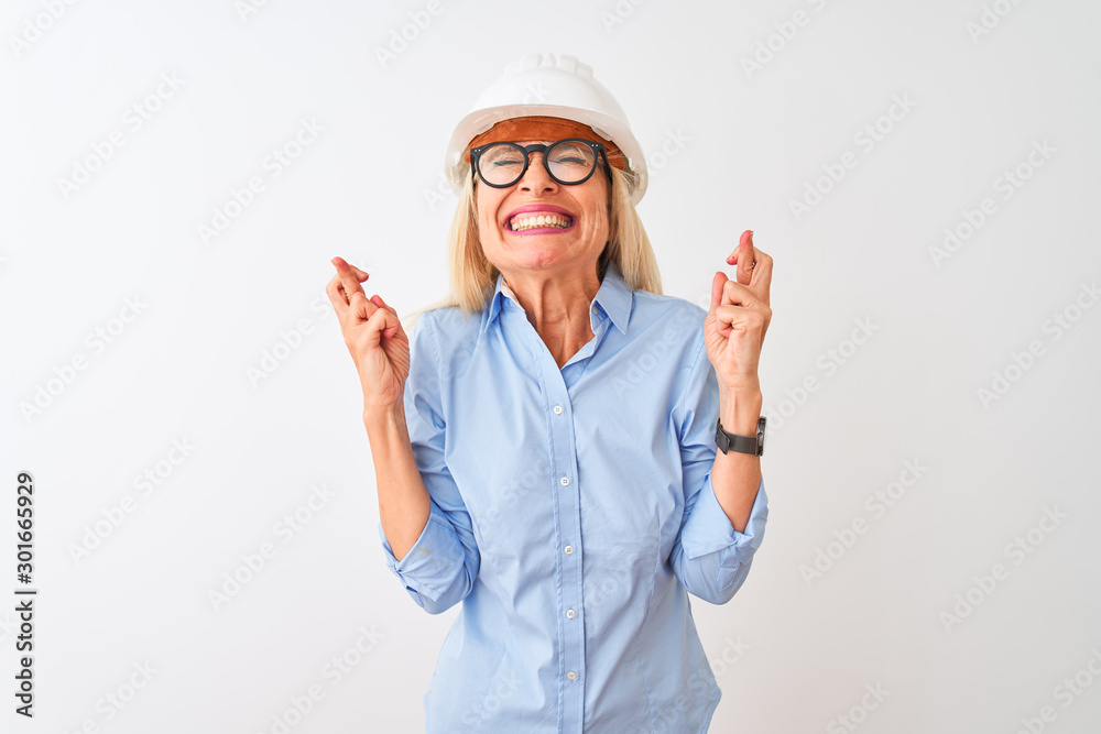 Middle age architect woman wearing glasses and helmet over isolated white background gesturing finger crossed smiling with hope and eyes closed. Luck and superstitious concept. Middle age architect woman wearing glasses and helmet over isolated white background gesturing finger crossed smiling with hope and eyes closed. Luck and superstitious concept.