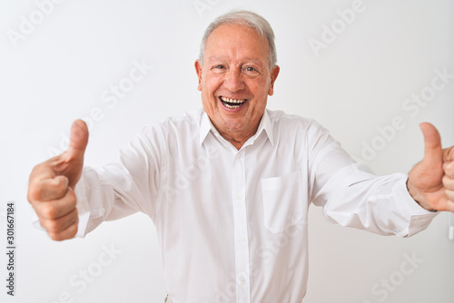 Senior grey-haired man wearing elegant shirt standing over isolated white background approving doing positive gesture with hand, thumbs up smiling and happy for success. Winner gesture.