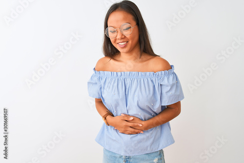 Young chinese woman wearing blue t-shirt and glasses over isolated white background with hand on stomach because indigestion, painful illness feeling unwell. Ache concept.