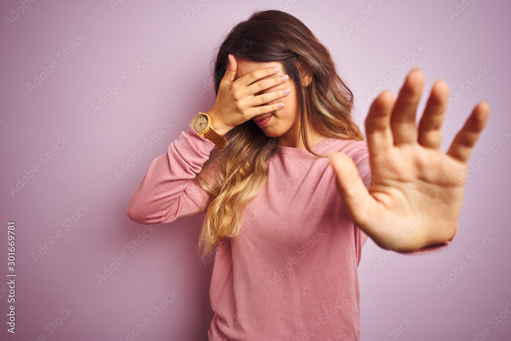 Young beautiful woman wearing a sweater over pink isolated background covering eyes with hands and doing stop gesture with sad and fear expression. Embarrassed and negative concept. Young beautiful woman wearing a sweater over pink isolated background covering eyes with hands and doing stop gesture with sad and fear expression. Embarrassed and negative concept.