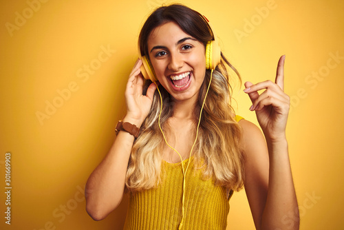 Young beautiful woman wearing headphones over yellow isolated background very happy pointing with hand and finger to the side