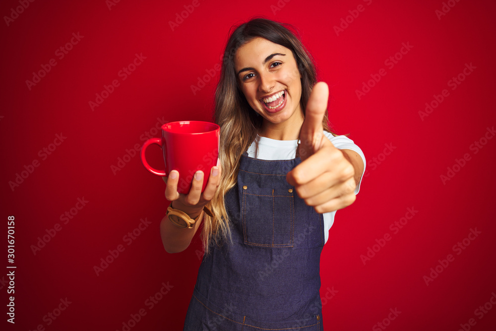 Young beautiful barista woman wearing apron over red isolated background happy with big smile doing ok sign, thumb up with fingers, excellent sign Young beautiful barista woman wearing apron over red isolated background happy with big smile doing ok sign, thumb up with fingers, excellent sign