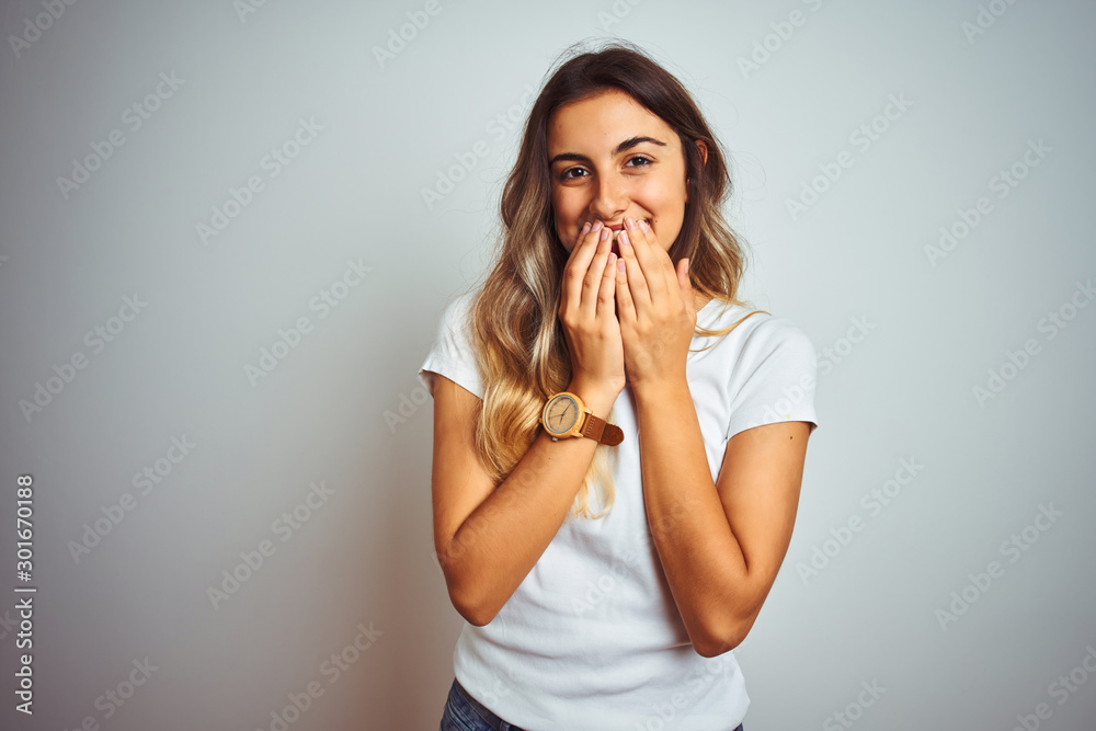 Young beautiful woman wearing casual white t-shirt over isolated background laughing and embarrassed giggle covering mouth with hands, gossip and scandal concept Young beautiful woman wearing casual white t-shirt over isolated background laughing and embarrassed giggle covering mouth with hands, gossip and scandal concept