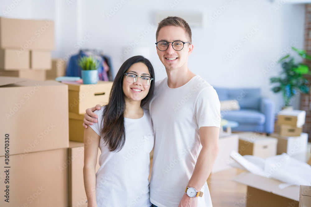 Young beautiful couple wearing glasses standing at new home around cardboard boxes Young beautiful couple wearing glasses standing at new home around cardboard boxes