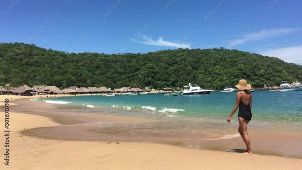 Woman walking down the beach enjoying the tropical surroundings, ocean and boats in water. Woman walking down the beach enjoying the tropical surroundings, ocean and boats in water.