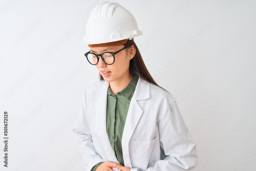 Young chinese engineer woman wearing coat helmet glasses over isolated white background with hand on stomach because indigestion, painful illness feeling unwell. Ache concept. Young chinese engineer woman wearing coat helmet glasses over isolated white background with hand on stomach because indigestion, painful illness feeling unwell. Ache concept.