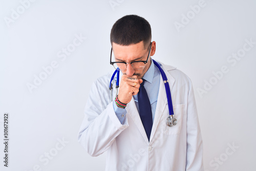 Young doctor man wearing stethoscope over isolated background feeling unwell and coughing as symptom for cold or bronchitis. Healthcare concept.