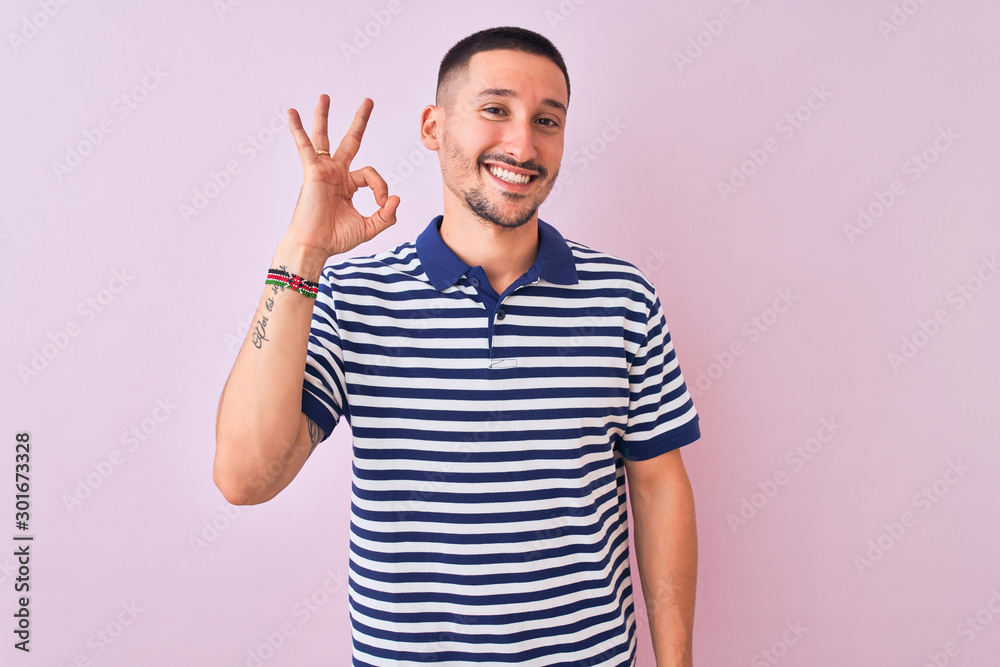 Young handsome man wearing nautical striped t-shirt over pink isolated background smiling positive doing ok sign with hand and fingers. Successful expression. Young handsome man wearing nautical striped t-shirt over pink isolated background smiling positive doing ok sign with hand and fingers. Successful expression.