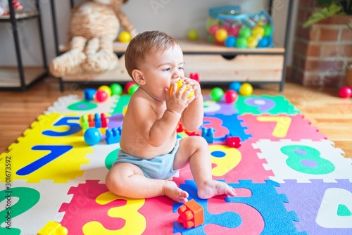 Beautiful toddler sitting on the puzzle carpet toy playing with colorful balls at kindergarten