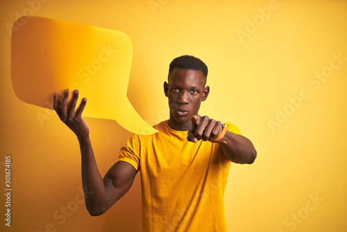 Young african american man holding speech bubble standing over isolated yellow background pointing with finger to the camera and to you, hand sign, positive and confident gesture from the front