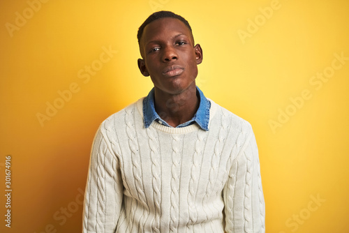 African american man wearing denim shirt and white sweater over isolated yellow background looking sleepy and tired, exhausted for fatigue and hangover, lazy eyes in the morning.