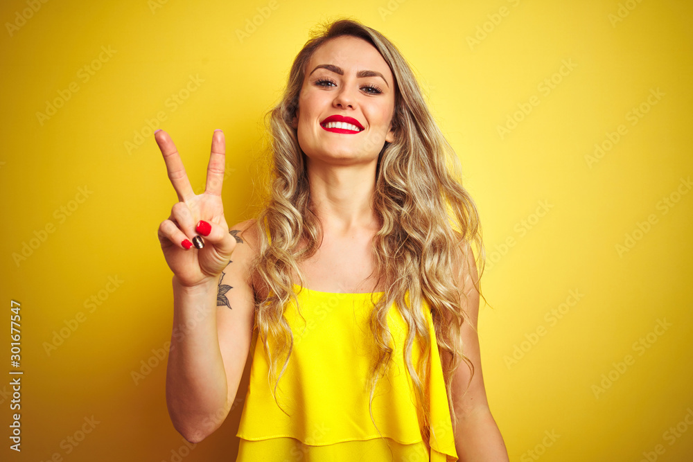 Young attactive woman wearing t-shirt standing over yellow isolated background showing and pointing up with fingers number two while smiling confident and happy. Young attactive woman wearing t-shirt standing over yellow isolated background showing and pointing up with fingers number two while smiling confident and happy.