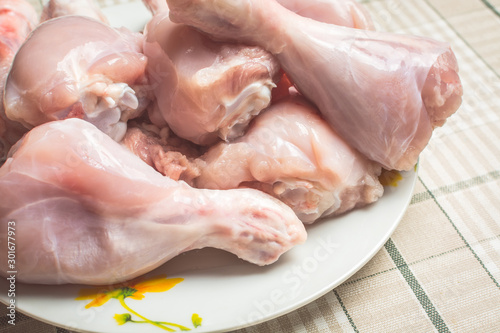 Raw chicken legs on a large plate drain from the water after washing.