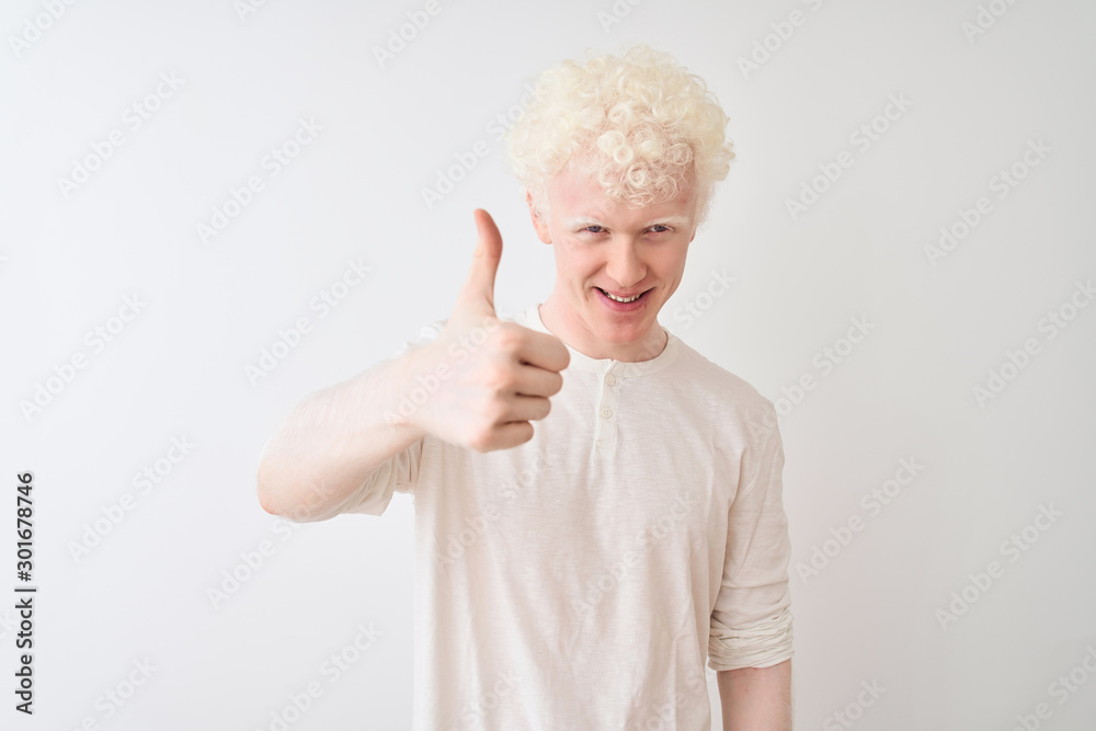Young albino blond man wearing casual t-shirt standing over isolated white background doing happy thumbs up gesture with hand. Approving expression looking at the camera showing success. Young albino blond man wearing casual t-shirt standing over isolated white background doing happy thumbs up gesture with hand. Approving expression looking at the camera showing success.