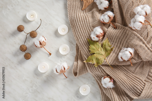 Warm sweater, beautiful cotton flowers, autumn leaf and candles on light background