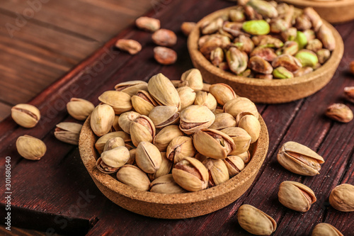 Bowls with tasty pistachio nuts on wooden background