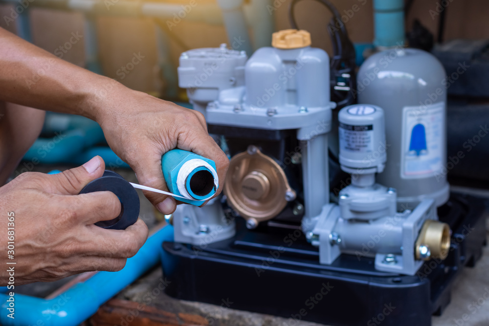 Plumber man hand using seal tape fitting with plastic pvc water pipeline with water pump machine blurred background. Maintenance concept. Plumber man hand using seal tape fitting with plastic pvc water pipeline with water pump machine blurred background. Maintenance concept.