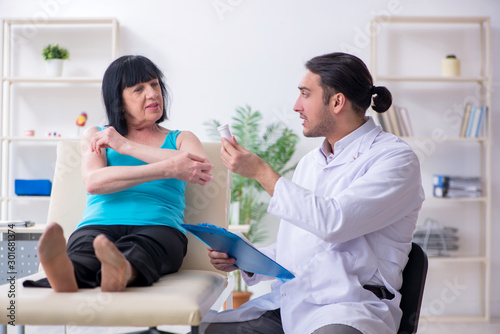 Young male doctor examining old female patient