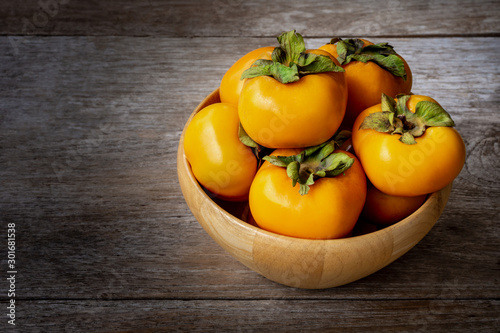 Fresh organic ripe Persimmons fruits in wooden bowl with slice isolated on old wooden table background. photo