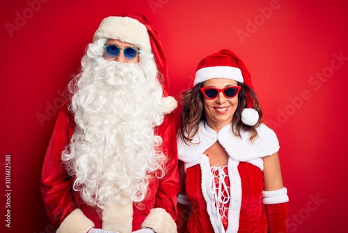 Middle age couple wearing Santa costume and sunglasses over isolated red background with a happy and cool smile on face. Lucky person.