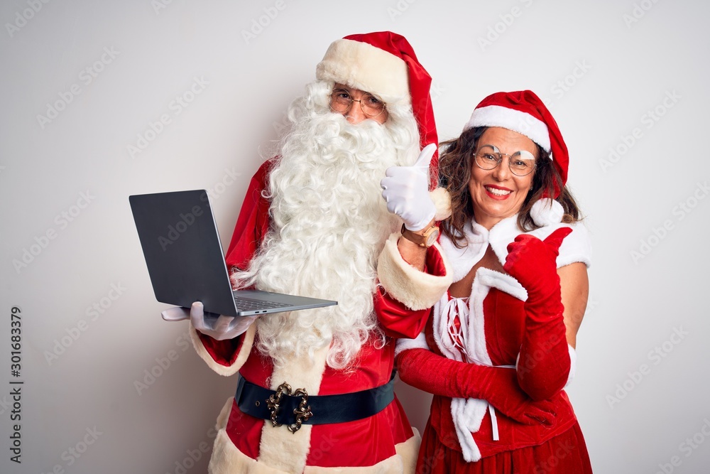 Senior couple wearing Santa Claus costume using laptop over isolated white background happy with big smile doing ok sign, thumb up with fingers, excellent sign Senior couple wearing Santa Claus costume using laptop over isolated white background happy with big smile doing ok sign, thumb up with fingers, excellent sign